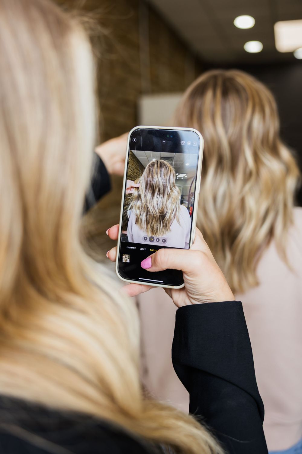 Person holding a mobile phone displaying a photo while taking pictures in an indoor setting.