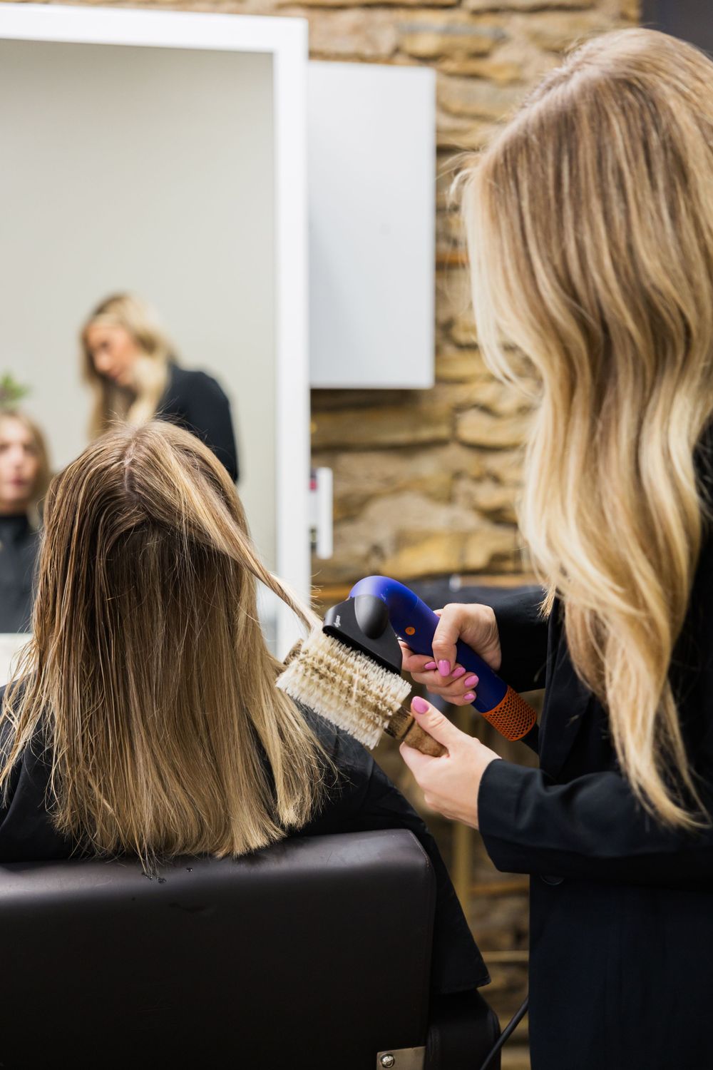 A series of photos showing blonde hair being styled and brushed at a salon with a stone wall background.