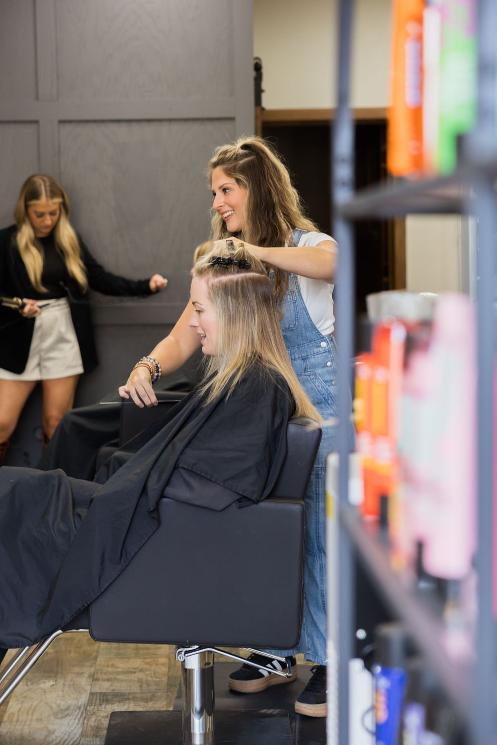 A client receives a professional hair styling service in a modern salon chair with blurred colorful background lighting.