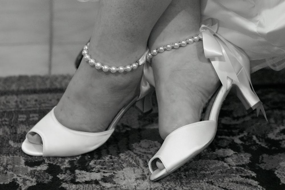 A series of black and white photos showing close-up details of white bridal shoes and pearls.