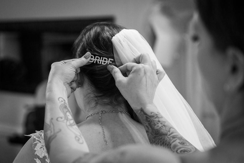 A bride getting her veil adjusted in a black and white wedding photograph.