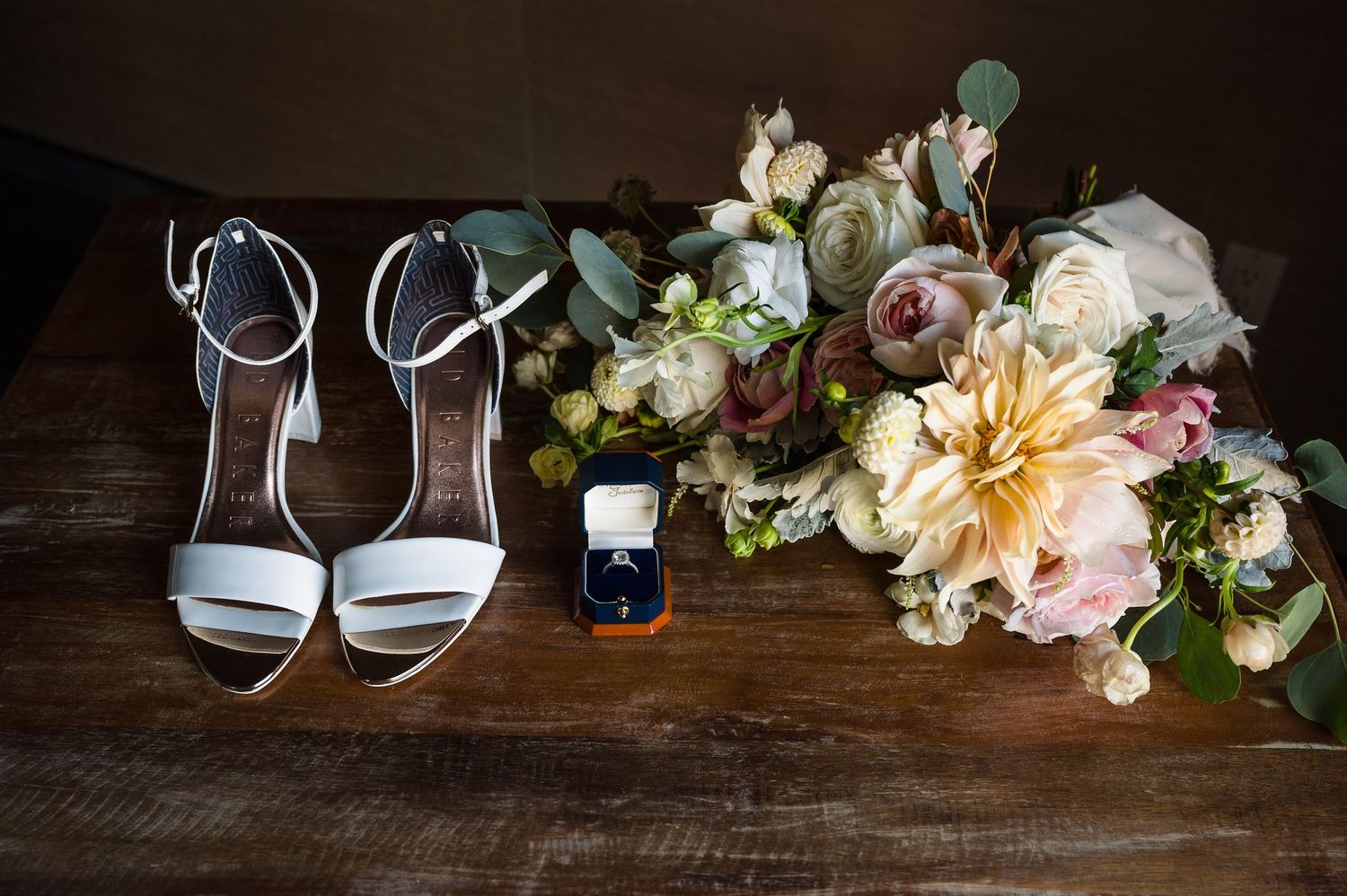 Wedding details including elegant shoes, delicate floral arrangements, and decorative elements on a rustic wooden surface.