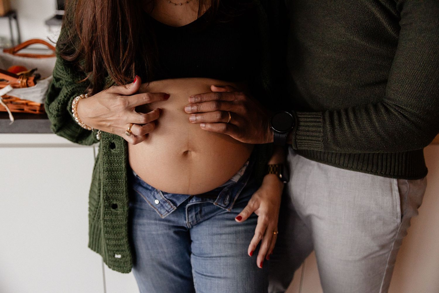 Couple tenderly cradles pregnant belly in a close-up maternity photo at home.