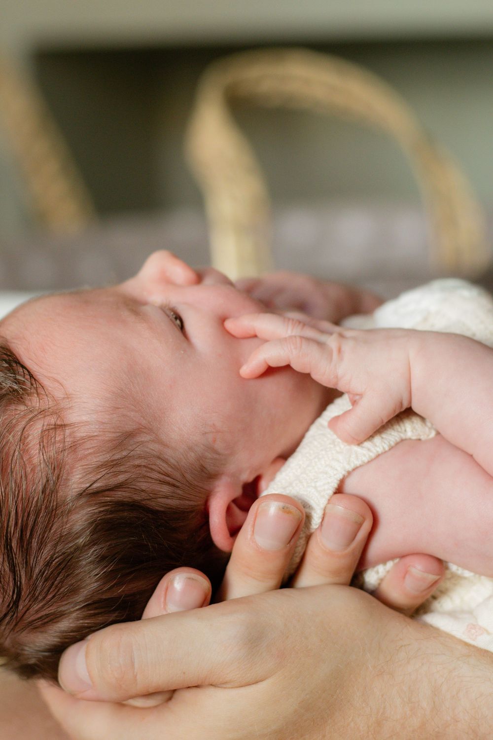 Close-up of a newborn baby being cradled in an adult's hands, wearing a white knit outfit.