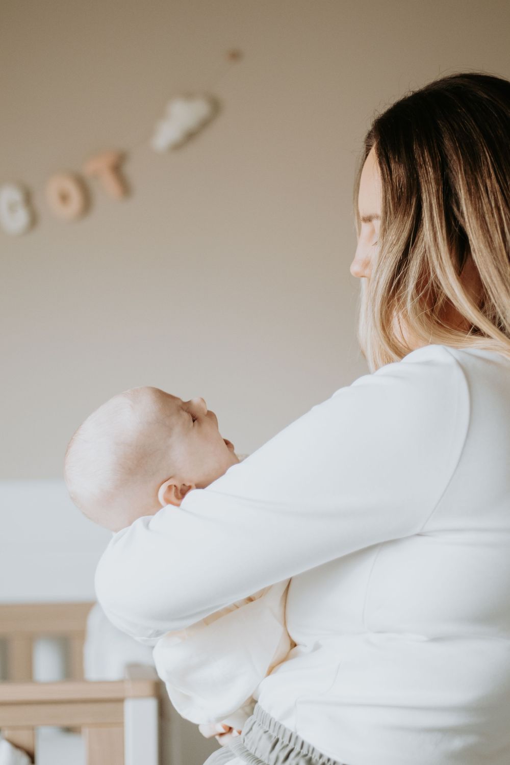 A gentle side view of someone in white holding a baby against their shoulder.