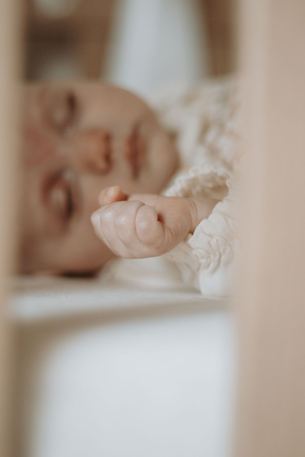 Peaceful sleeping baby with tiny hand visible through crib slats.