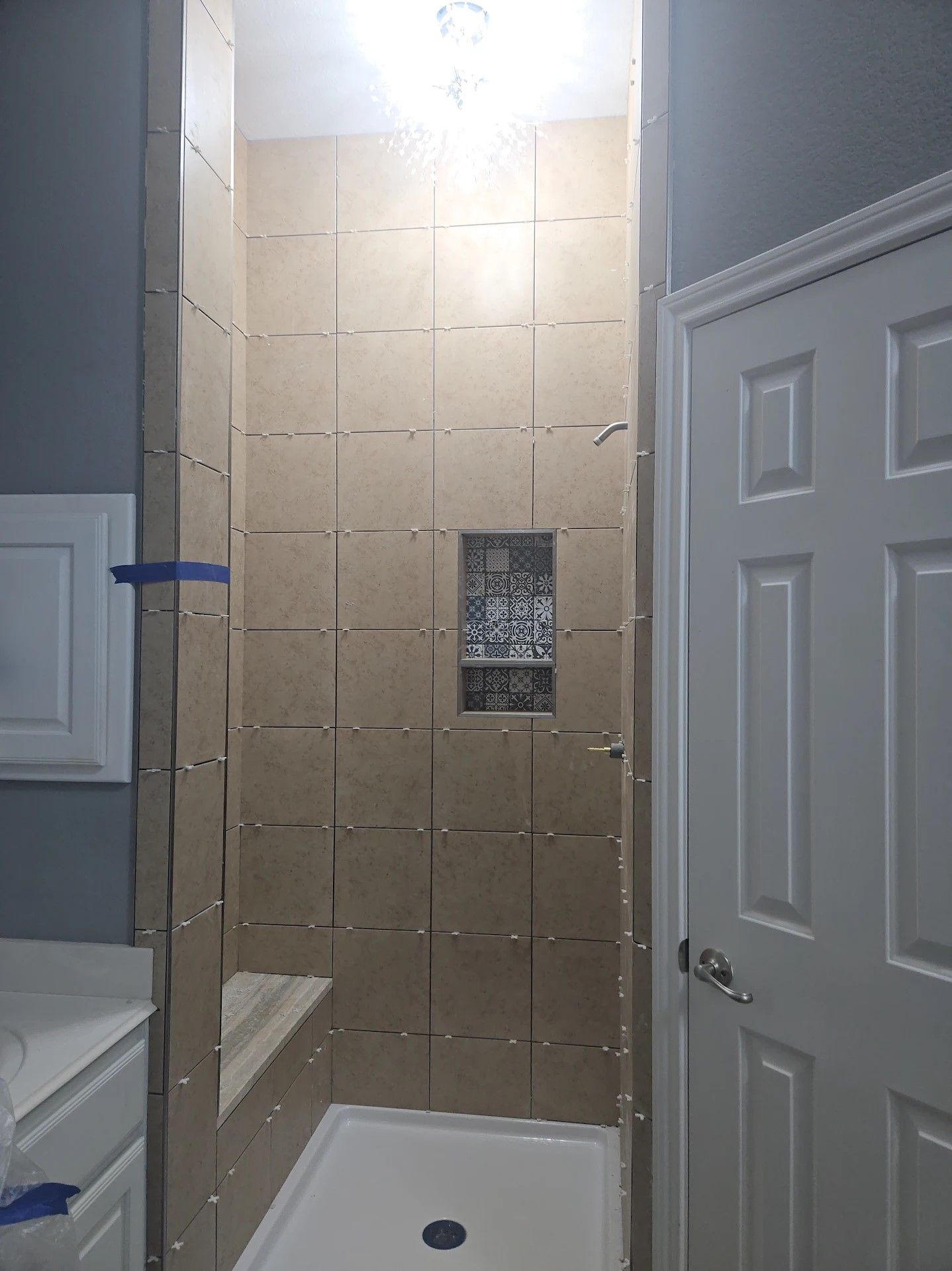 Narrow hallway with white doors and grey walls showing a bathroom renovation in progress with exposed tile work.