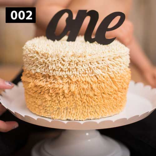 Elegant ombre cake decorated with textured buttercream frosting and black 'one' topper.