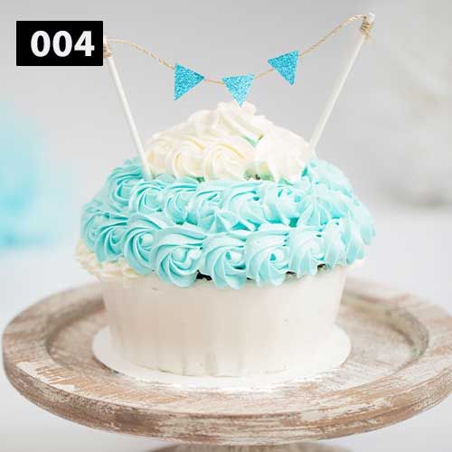 Turquoise and white smash cake with mini bunting topper on rustic wooden plate.