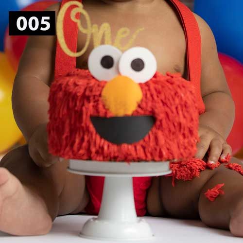 Elmo-themed smash cake with red frosting and googly eyes on a white cake stand.