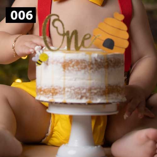 White birthday cake with gold 'One' topper displayed on a white pedestal stand.