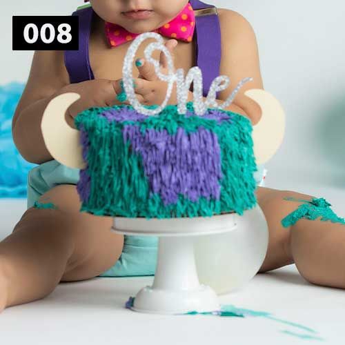 Turquoise and purple frosted smash cake with 'One' topper on white stand.