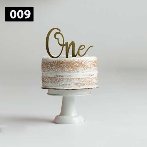 Simple white cake with elegant gold 'One' topper on white pedestal stand.