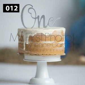 Minimalist tan frosted cake with silver 'One' topper on white pedestal.