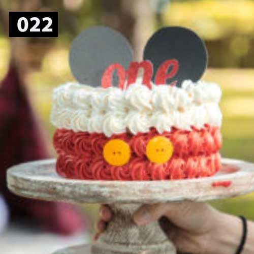 Red and white frosted cake decorated with yellow buttons on rustic cake stand.