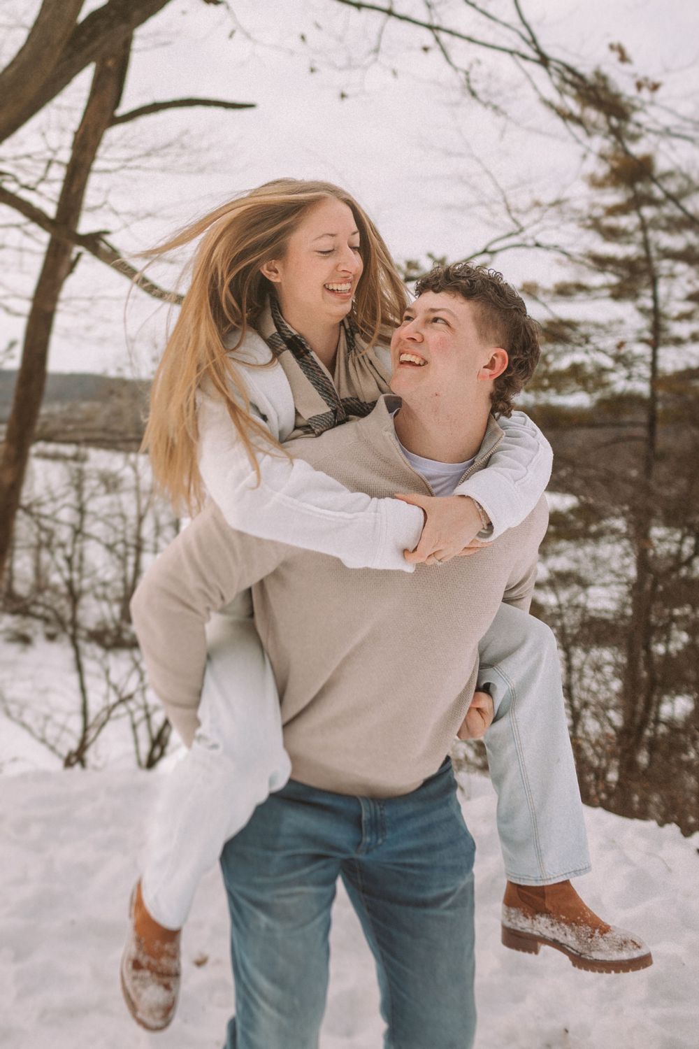 A couple playfully enjoying a winter day together in the snow with matching light-colored outfits.