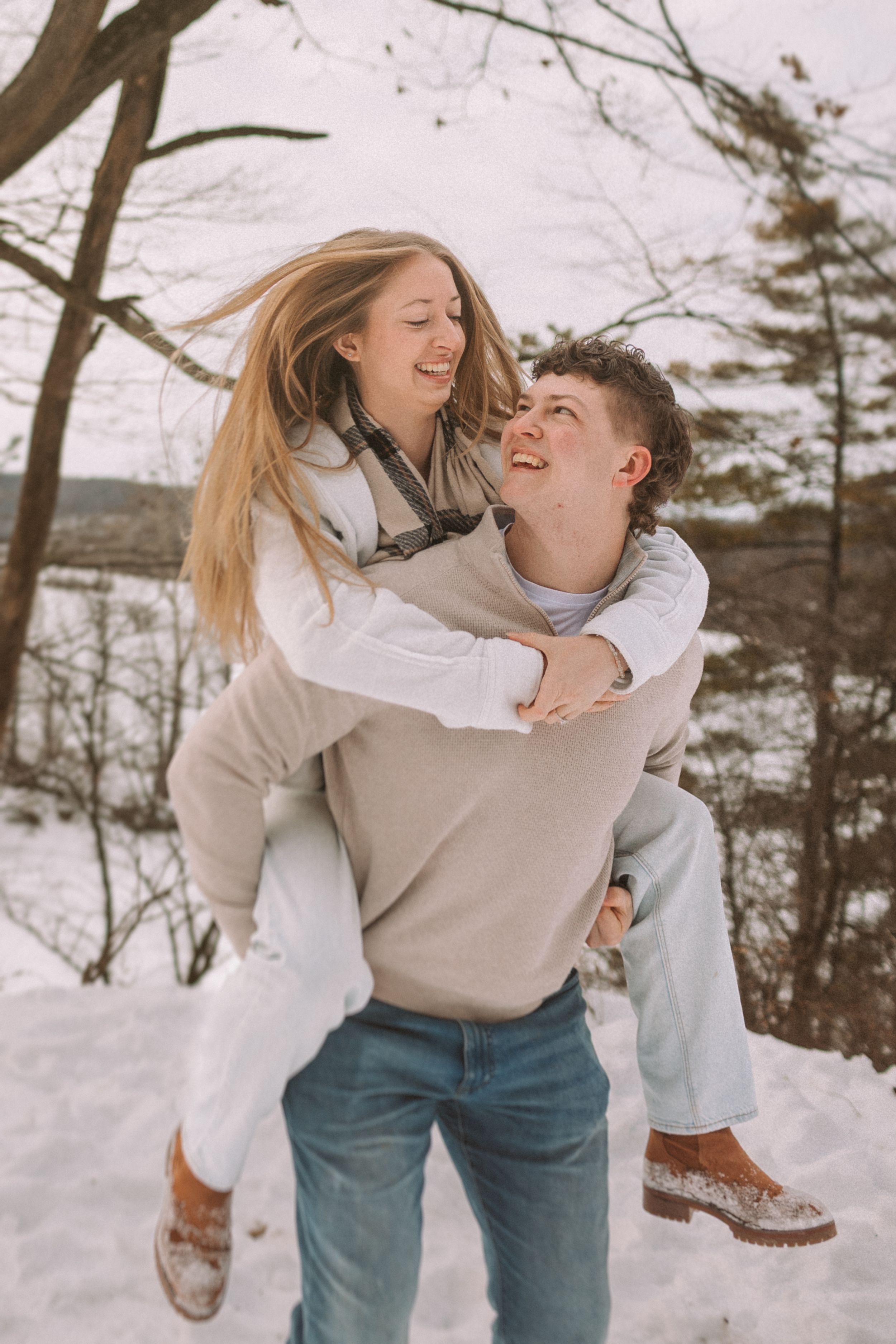 A couple playfully enjoying a winter day together in the snow with matching light-colored outfits.