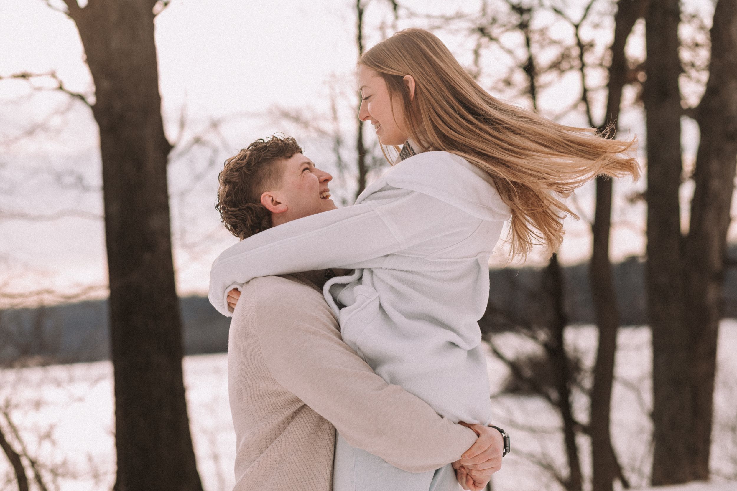 A romantic moment captured between two people hugging against a snowy winter backdrop.