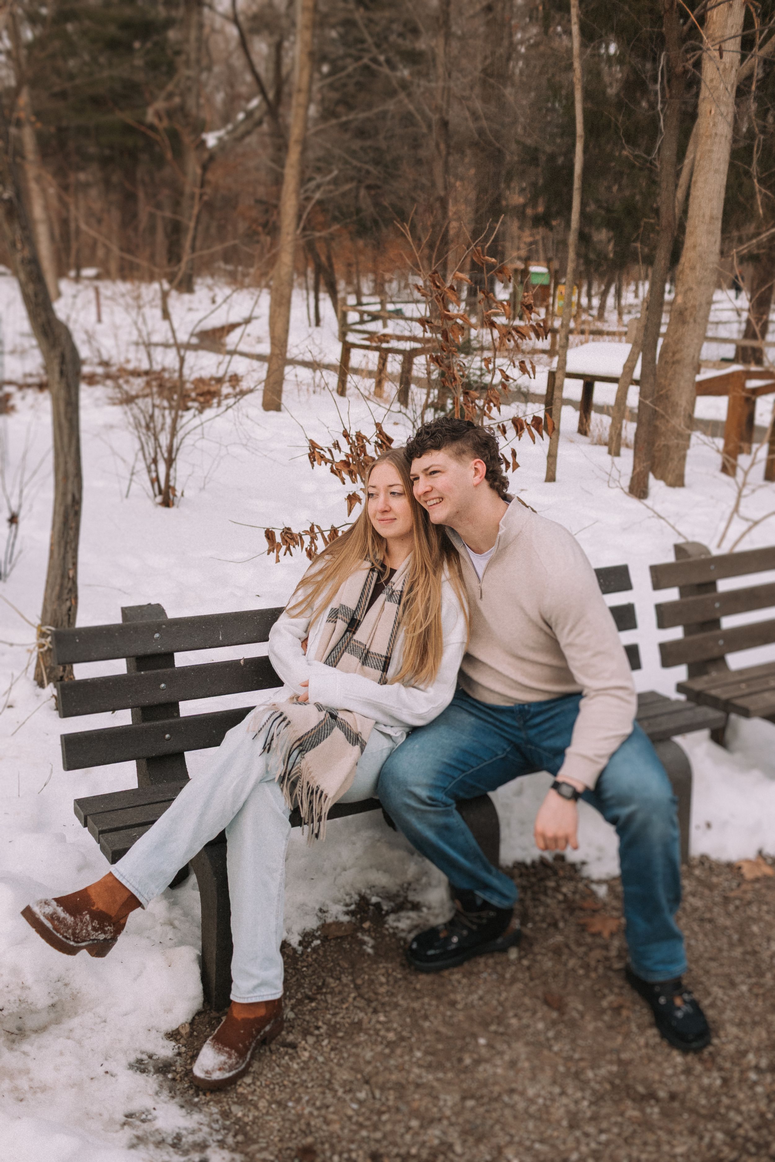 Couple sitting together on wooden bench in snowy winter forest setting sharing playful moments.