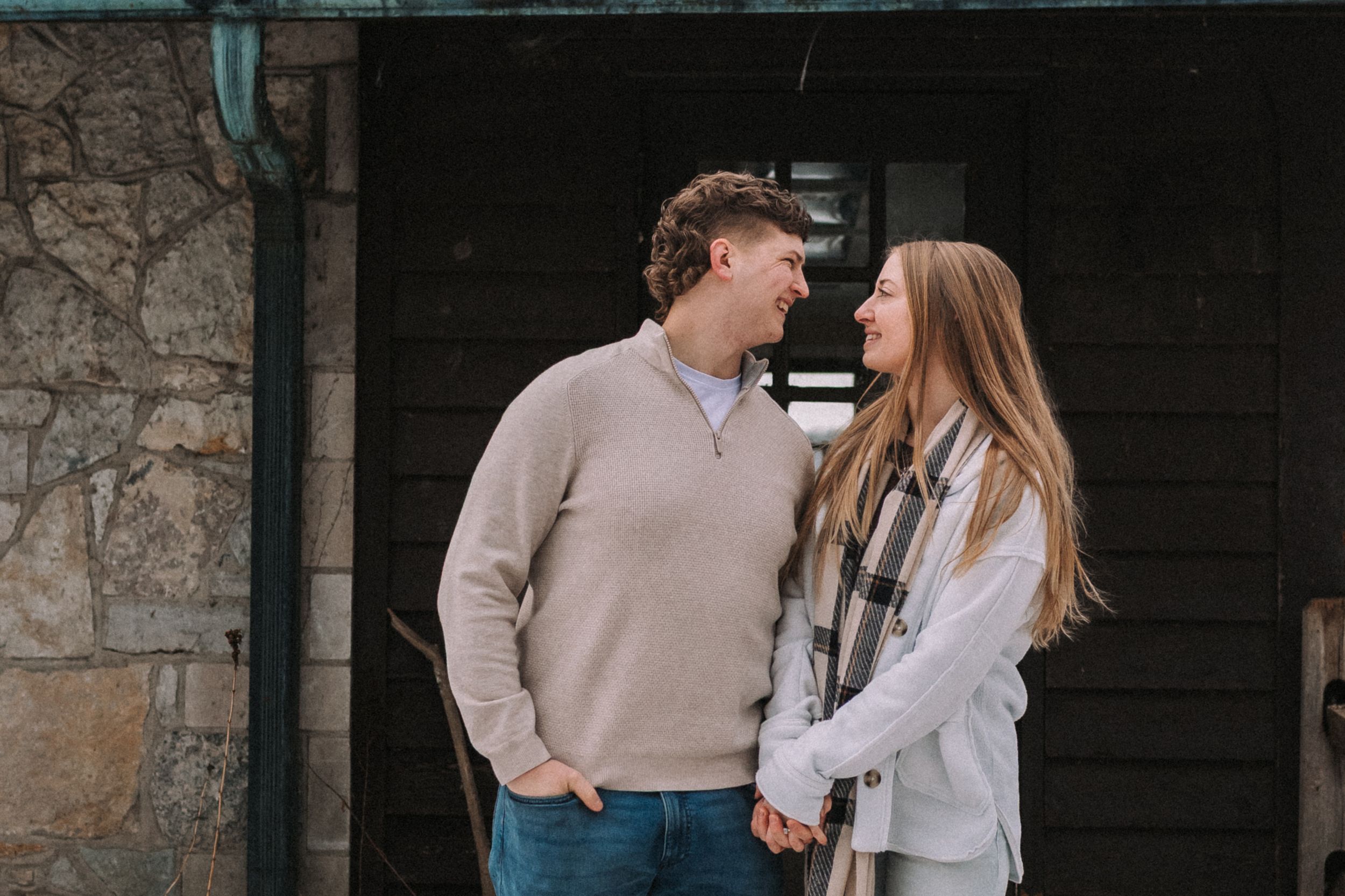 A couple sharing intimate moments and laughter against a rustic stone wall background.