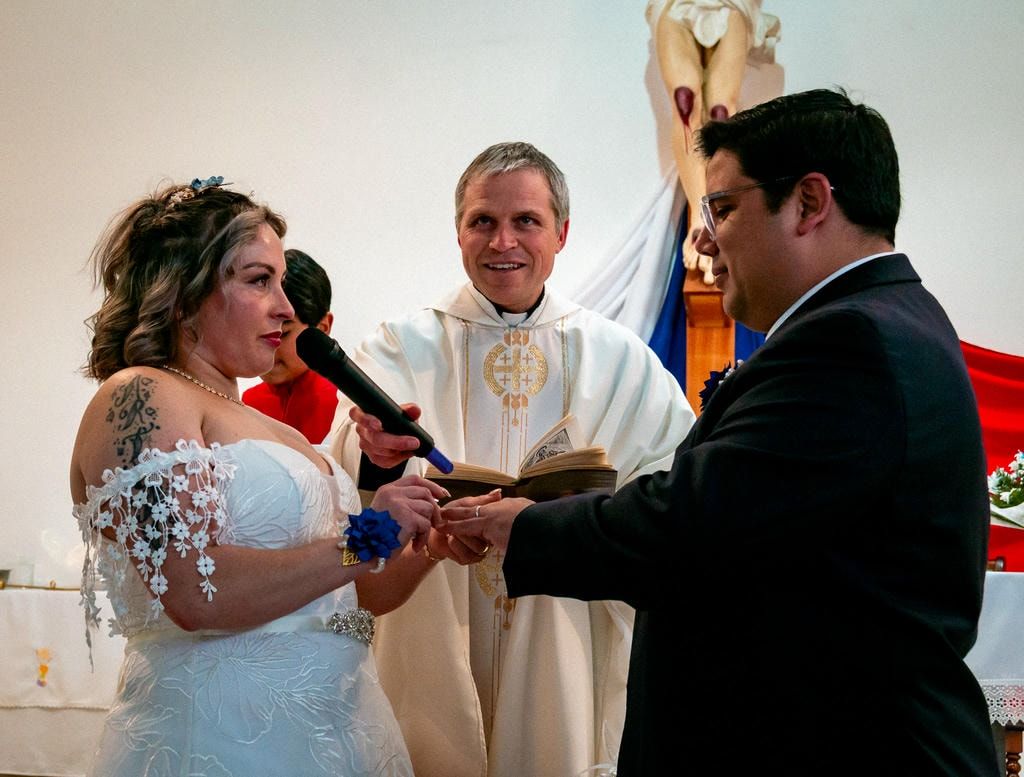 Ceremonia de matrimonio con sacerdote oficiando mientras la pareja intercambia anillos.