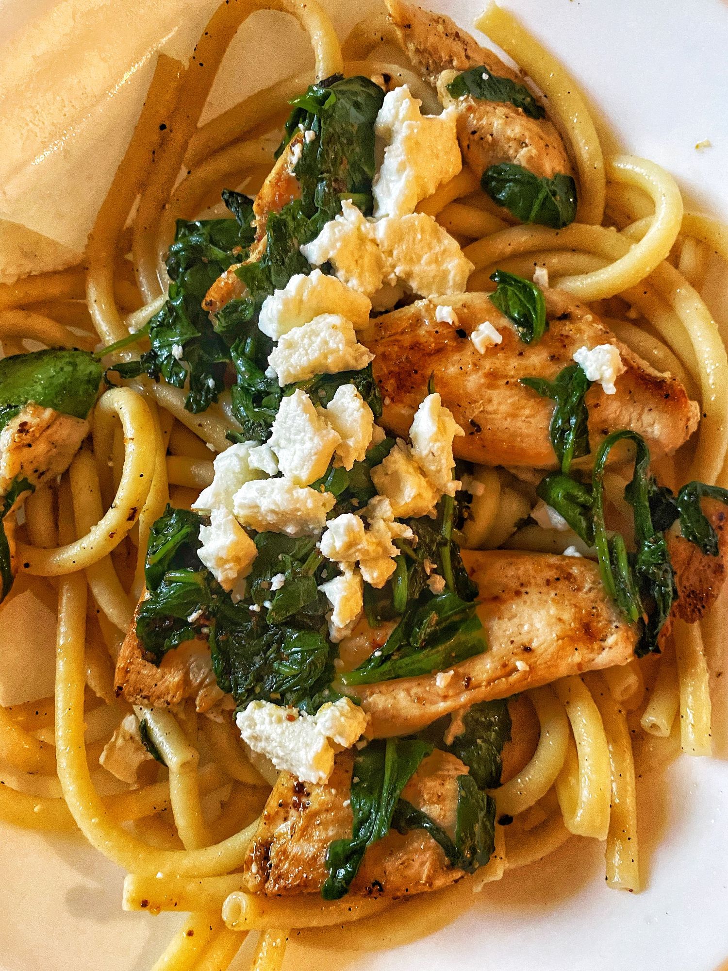 Bucatini pasta dish topped with sauteed mushrooms, wilted spinach, and crumbled feta cheese in a light sauce.