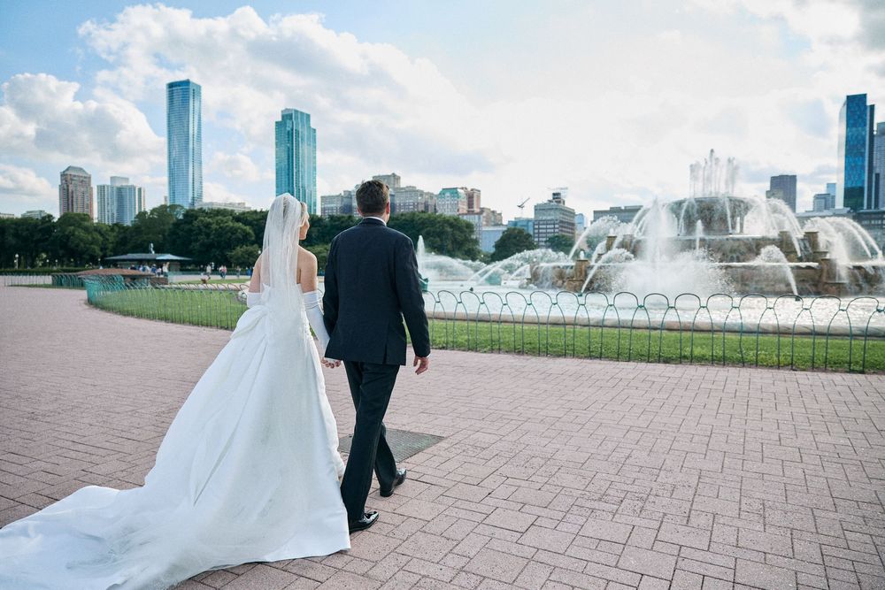 A couple in wedding attire poses near Buckingham Fountain in Chicago's Grant Park with the city skyline behind them.