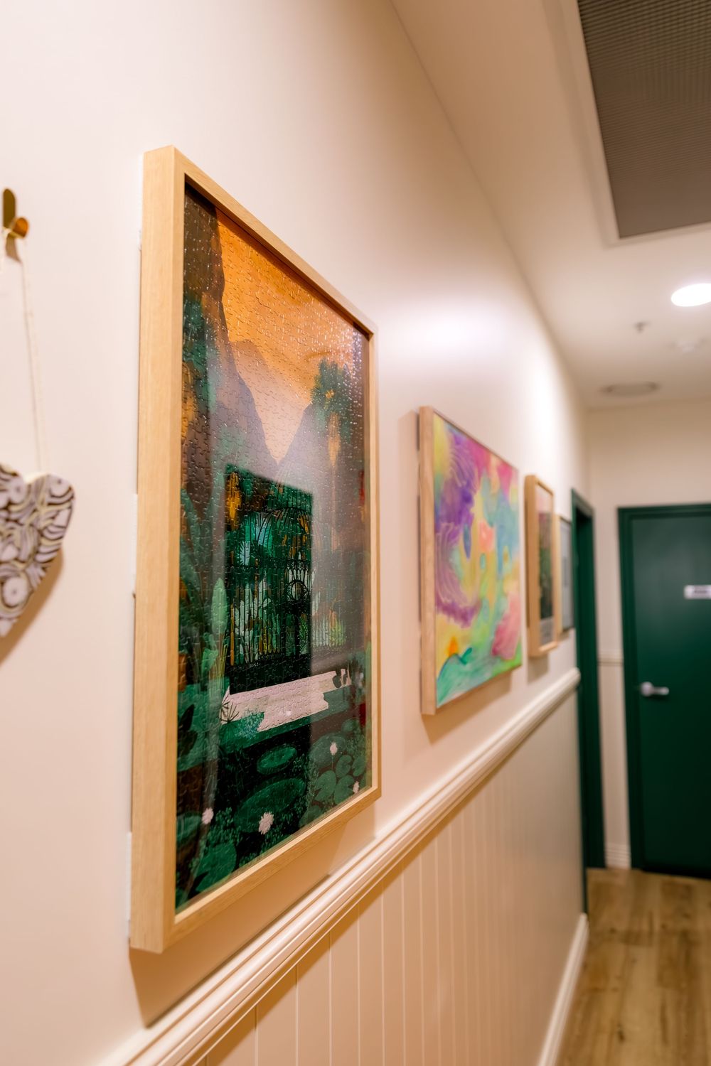 Framed artwork displayed along a white hallway wall with soft lighting illuminating the gallery-style space.