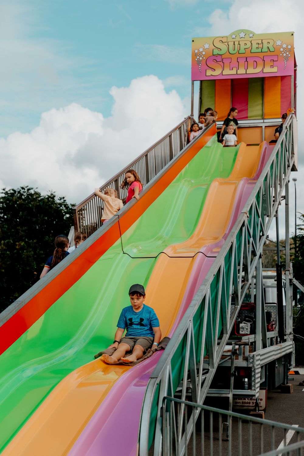 Children enjoying a colorful rainbow slide at a carnival fair with multiple lanes for racing down.