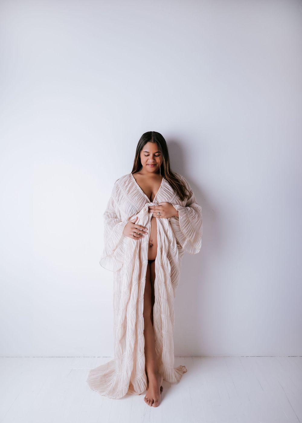 Ethereal maternity portraits in sheer white robe against minimal backdrop.