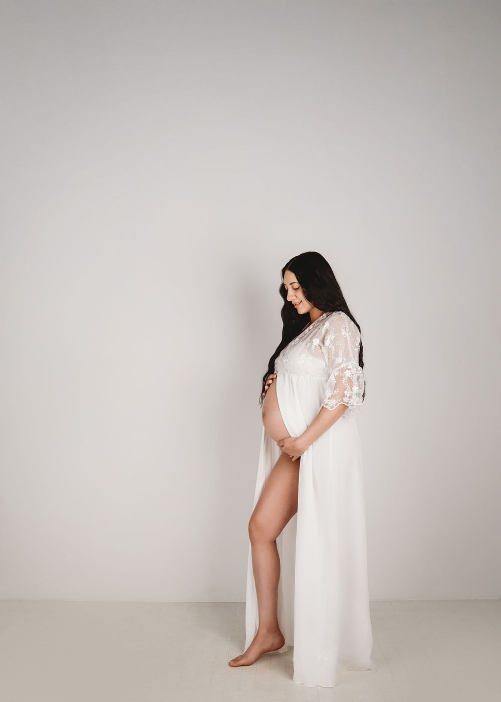 Minimalist maternity photos against white backdrop showing silhouette in flowing dress.