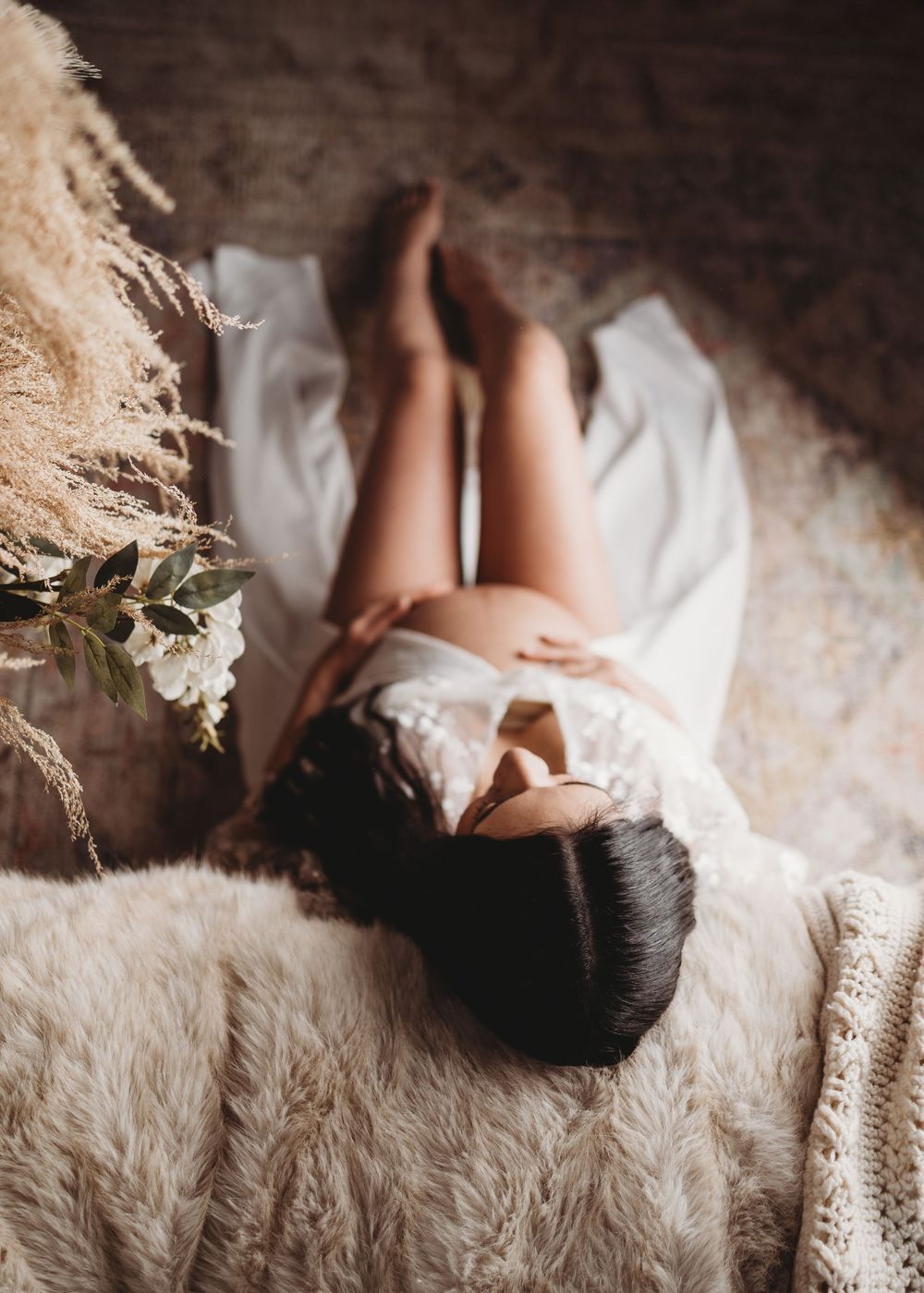 Artistic maternity photo shoot on white fluffy rug in natural light.