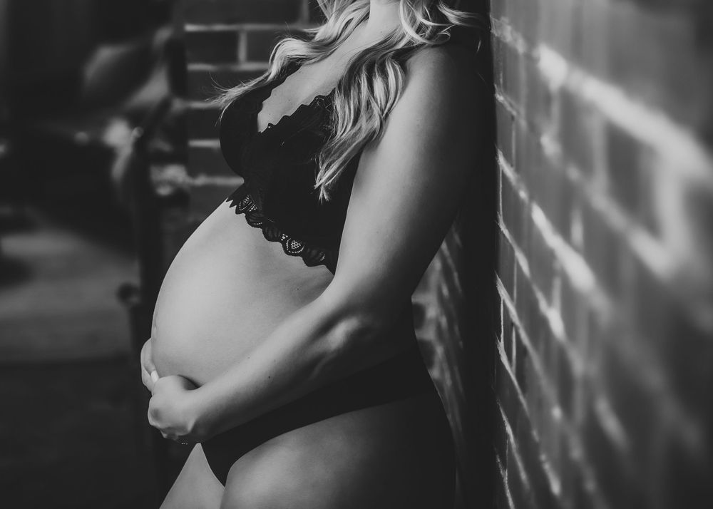Black and white maternity photos with dramatic window lighting.