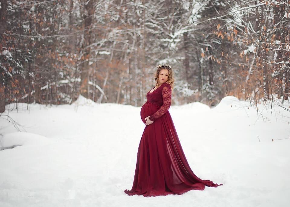 Dramatic winter maternity photos featuring a flowing burgundy dress in snowy forest.