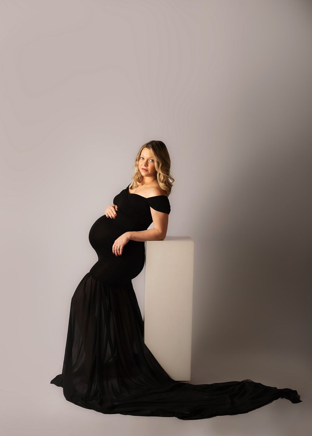 Maternity photoshoot featuring a flowing black dress against a neutral studio backdrop.