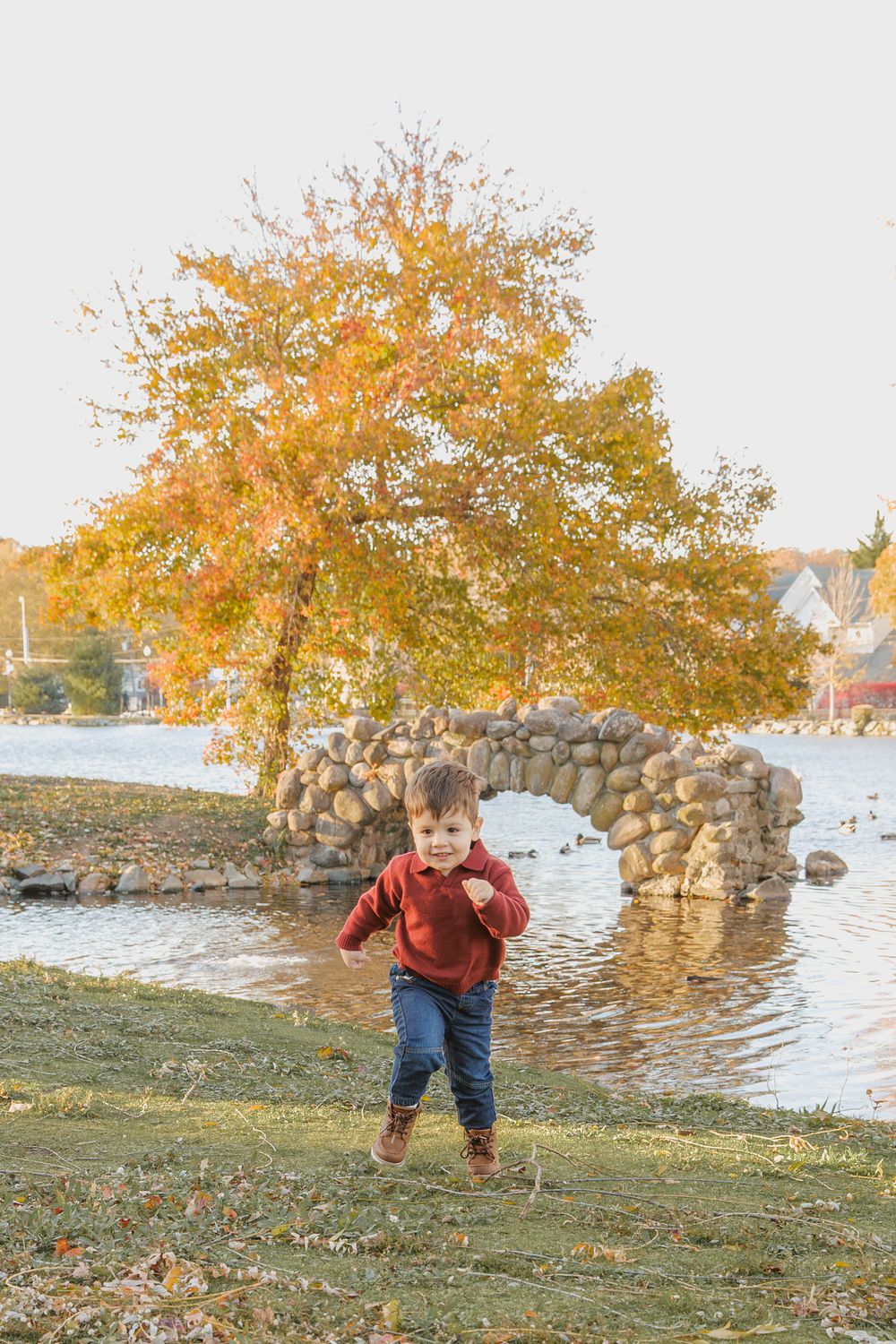 A small child explores a scenic autumn lakeside with golden trees and a stone wall on a crisp fall day.