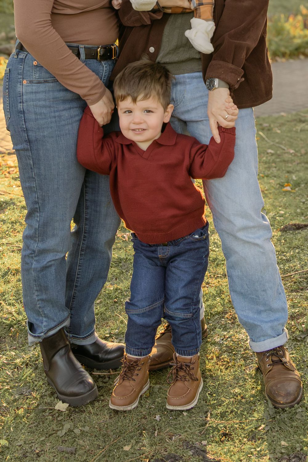 Family wearing matching brown leather boots and jeans standing together on grass in autumn.