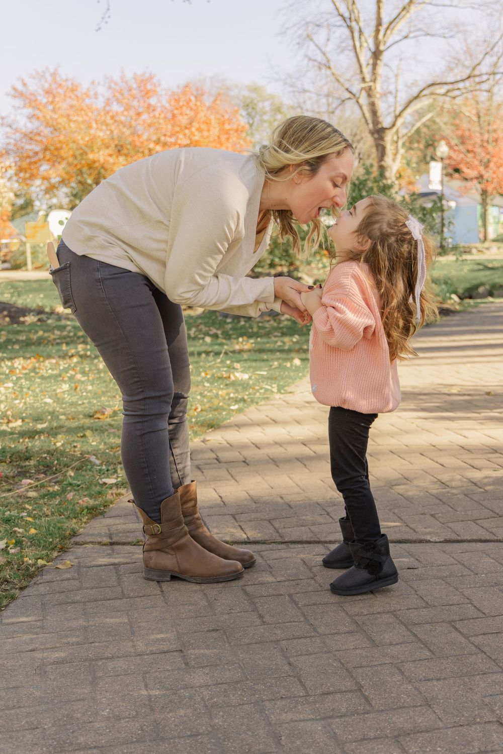 Two people share a joyful moment together on a brick pathway surrounded by autumn trees and fallen leaves.