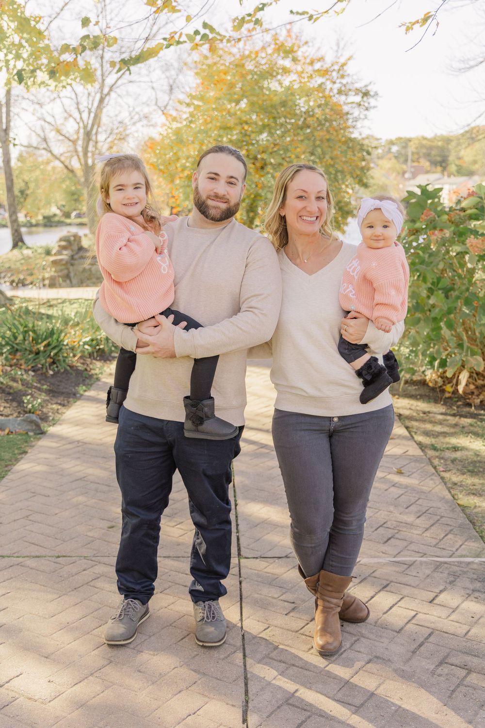 A family wearing coordinated neutral outfits poses together on a brick path during autumn.