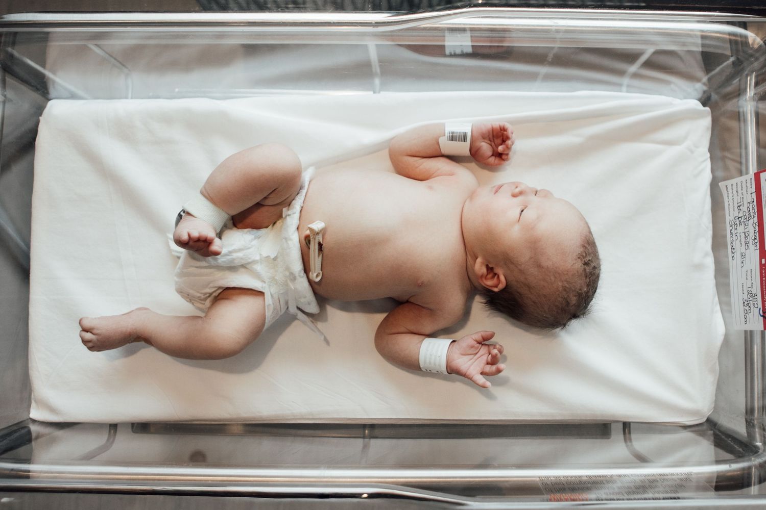 A newborn baby lies on a white medical examination table while being measured for growth and development.