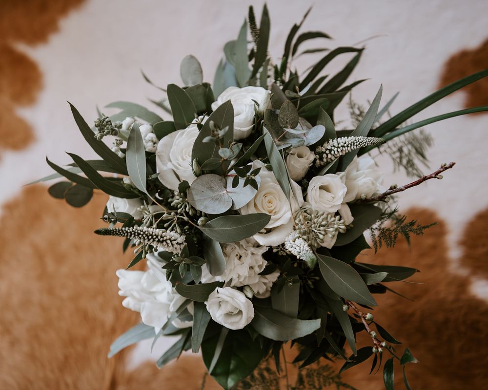 Romantic bridal bouquet featuring white roses, ranunculus, and lush greenery on a cowhide background.