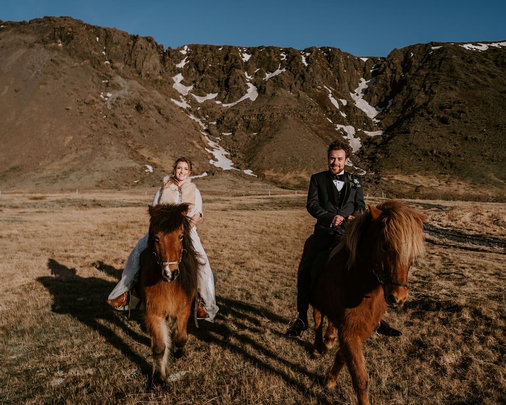 Bride and groom riding Icelandic horses together across a scenic mountain landscape.