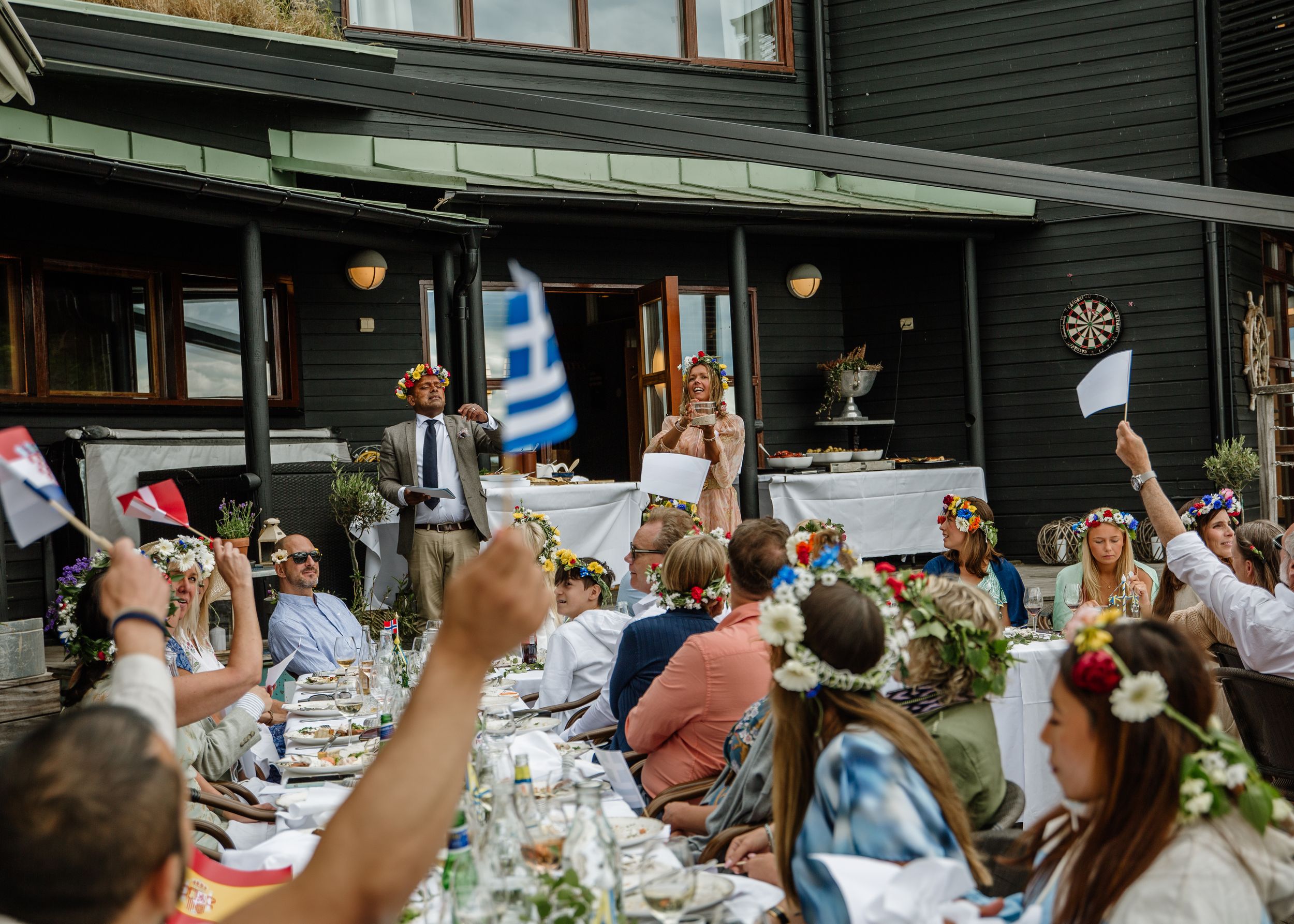 Outdoor wedding reception with guests raising flags and flowers at a long decorated table.