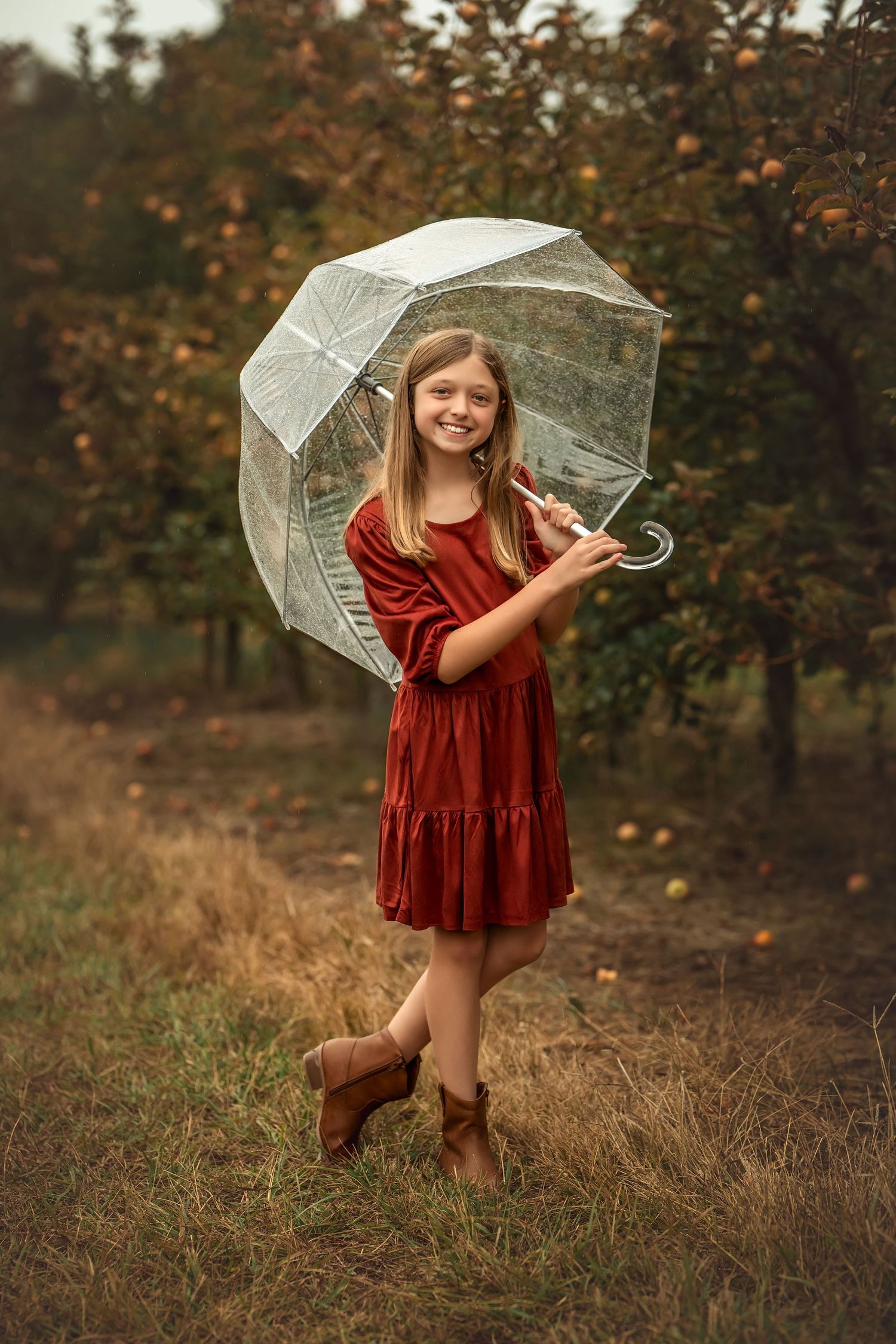 A young person in a burgundy velvet dress plays with a sheer white umbrella in an autumn field at sunset.
