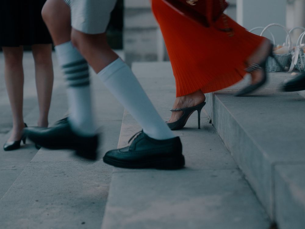 Dancers in white socks and black shoes performing synchronized movements on a grey floor.