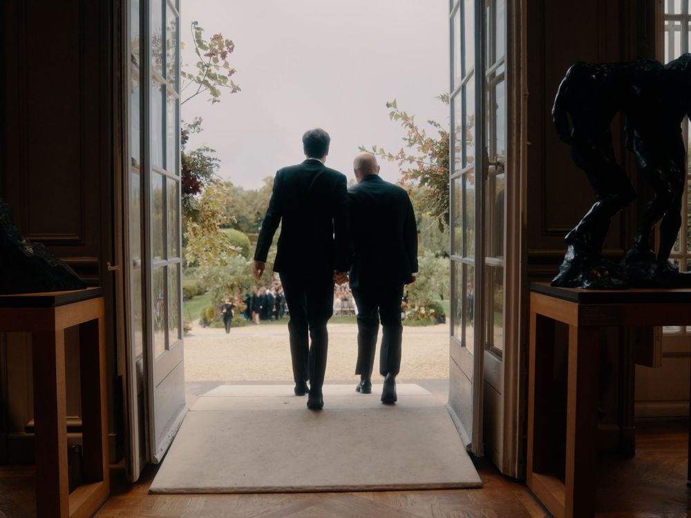 Two figures walk down a long corridor with natural light streaming in from tall windows.