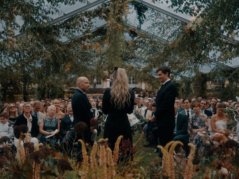 Outdoor wedding ceremony setup with wooden chairs and floral arrangements in a garden setting.