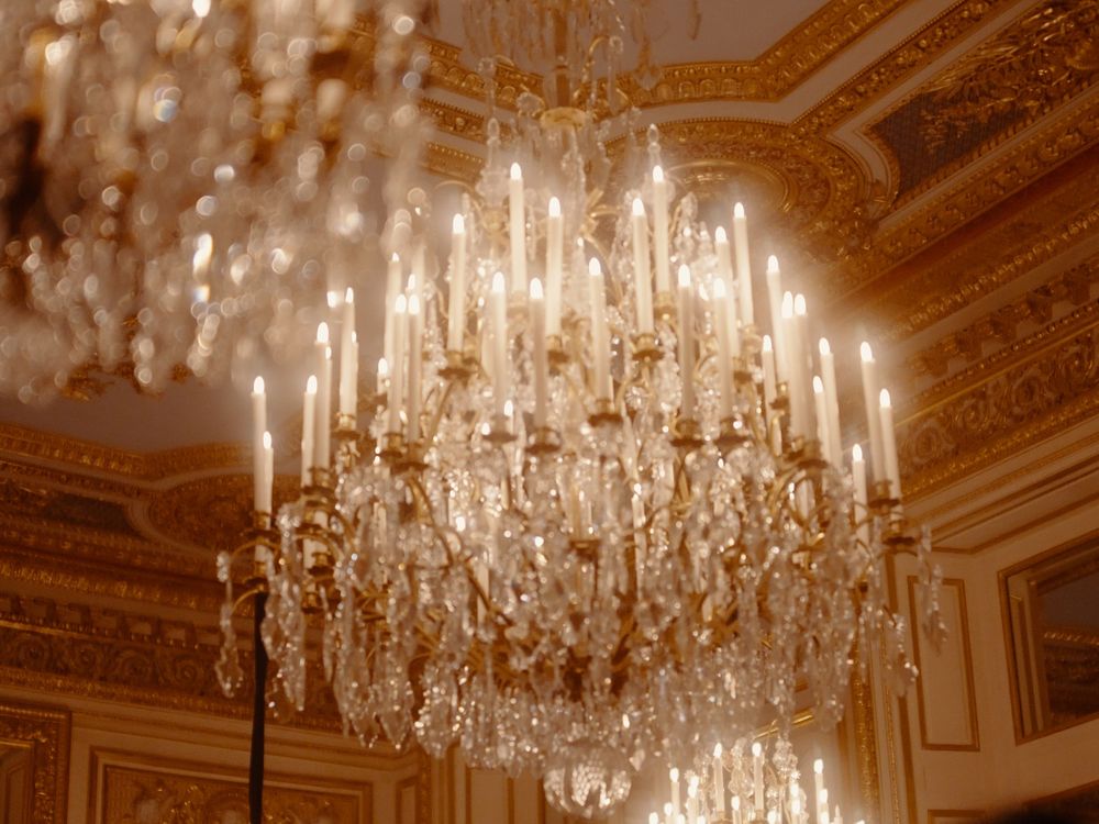 Ornate crystal chandeliers hanging from an elegant gold-trimmed ceiling in a grand ballroom.