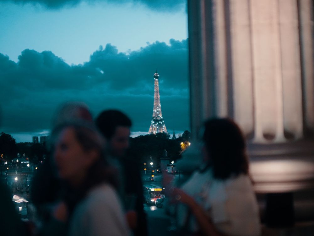 Cityscape at dusk with blurred lights and architectural silhouettes against a blue sky.