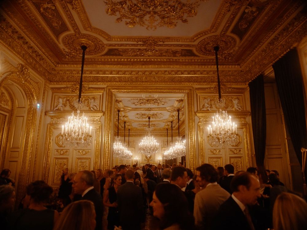 Ornate crystal chandeliers illuminate a grand baroque ballroom with gilded walls and intricate ceiling details.